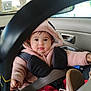 baby, child, car_seat, seat_belt, hoodie, pink_clothing, car_interior, steering_wheel, cute, infant, safety, seatbelt, window, tree, door_handle, clothing, person, portrait, face, young_child