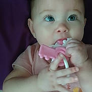Amira is registered to the contest to win money with this photo: baby, infant, blue_eyes, pink_onesie, toy, teething_toy, lying_down, curious, child, cute, young_child, hand, face, skin, indoor, soft_lighting, expression, closeup, portrait, childhood