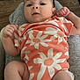 baby, infant, onesie, orange_clothing, daisy_pattern, soft_surface, grey_fabric, wooden_floor, curious_expression, small_hands, lying_down, indoor, person, child, cute, portrait, casual, comfortable, young, innocent