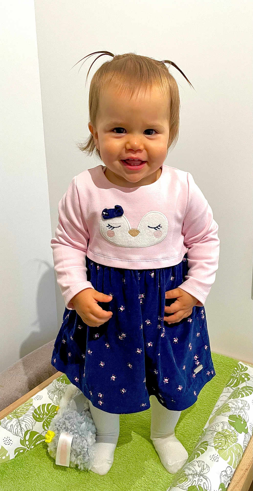 Lana a rejoint le concours — aidez-le/la à gagner de superbes lots ! toddler, child, smiling, standing, indoor, dress, pink, navy_blue, pigtails, toy, stuffed_animal, white_tights, green_cushion, happy, cute, person, portrait, small_child, playful, clothing
