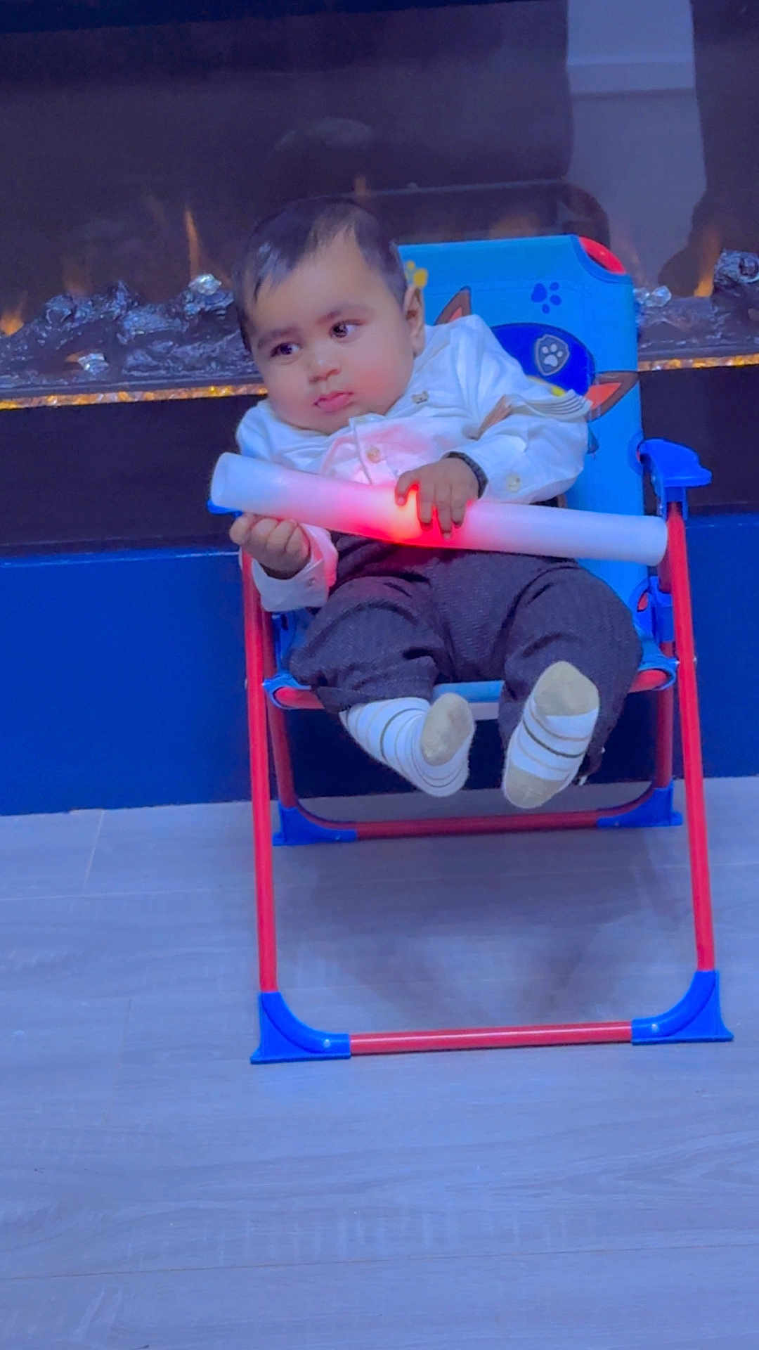 Munraj is registered to the contest to win money with this photo: baby, child, chair, light_stick, indoor, floor, socks, pants, shirt, face, hands, toy, fireplace, blue, red, comfort, seated, expression, person, home