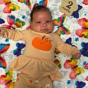 Layla is registered to the contest to win money with this photo: baby, infant, child, blanket, butterfly, colorful, clothing, pumpkin, cute, wooden_sign, 2_months, laying_down, portrait, face, smile, soft, pattern, fabric, sleepwear, newborn