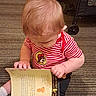 Ronin joined the competition — help win amazing prizes! baby, child, toddler, reading, book, picture_book, striped_shirt, red_clothing, sitting, carpet, indoor, stroller, infant, blond_hair, looking_down, hands, sock, portrait, family, cute