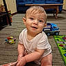 baby, child, infant, sitting, smiling, portrait, face, indoors, living_room, carpet, couch, toy, toy_truck, play_mat, blanket, onesie, red_ball, colorful, happy, family_home