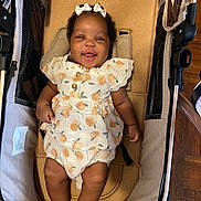 Kiara joined the competition — help win amazing prizes! baby, baby_girl, bow, child, closeup, clothing, curly_hair, cute, fabric, footwearless, happy, indoor, infant, patterned_outfit, person, relaxing, seat, skin, smiling, stroller
