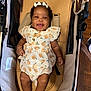 baby, baby_girl, bow, child, closeup, clothing, curly_hair, cute, fabric, footwearless, happy, indoor, infant, patterned_outfit, person, relaxing, seat, skin, smiling, stroller