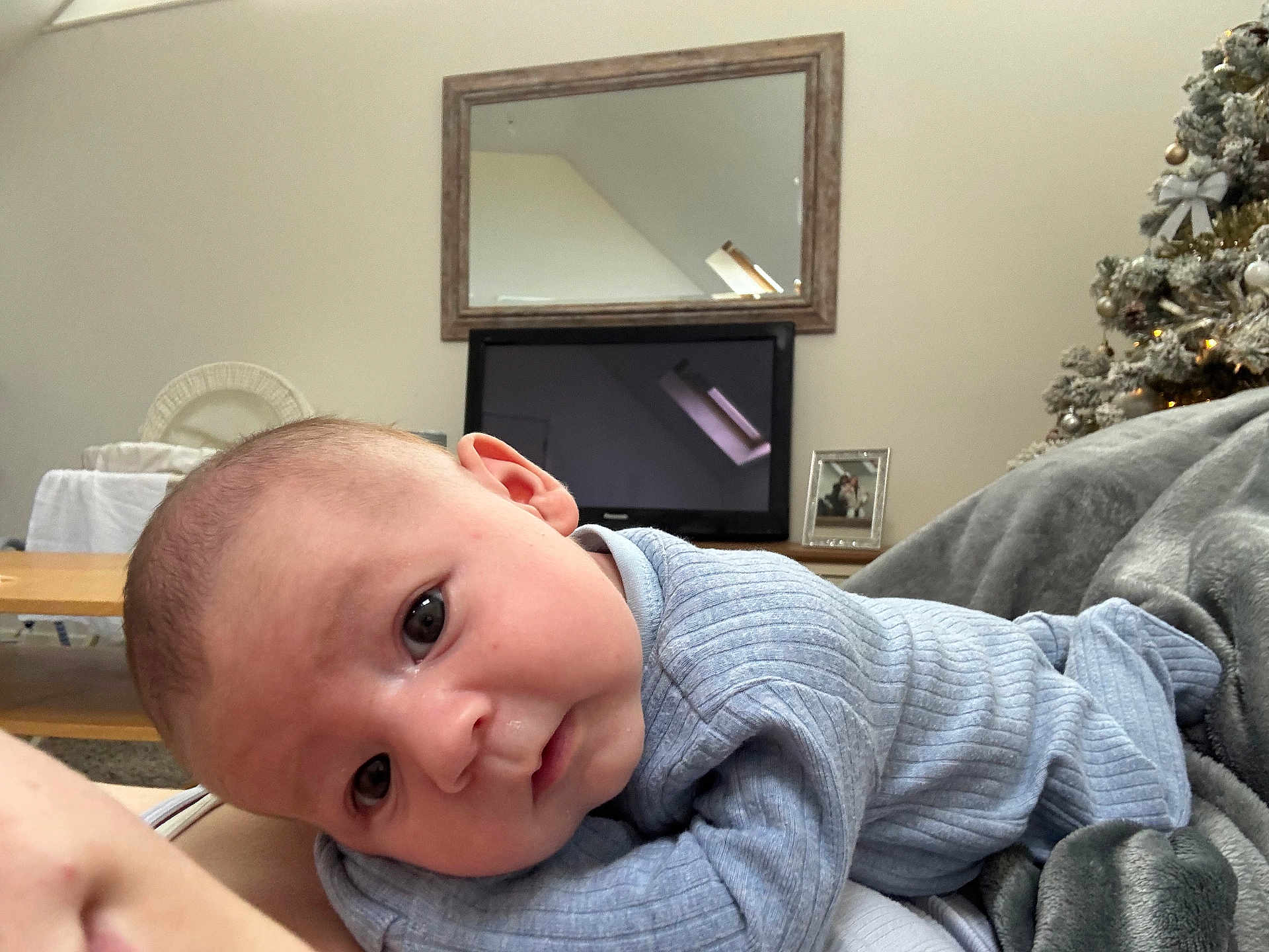 Louie-George joined the competition — help win amazing prizes! baby, infant, blue_clothing, blanket, face, head, eyes, indoor, television, mirror, christmas_tree, ornaments, furniture, cozy, portrait, person, soft_texture, table, picture_frame, home