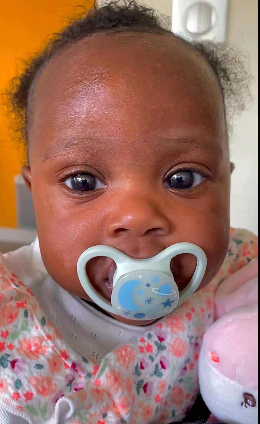 Theresa participe au concours pour gagner de l'argent avec cette photo : baby, pacifier, face, close_up, child, infant, plush_toy, pink, floral_pattern, cute, indoors, portrait, young_child, soft_toy, apparel, expression, skin, eyes, head, clothing