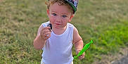 Nico is registered to the contest to win money with this photo: blue_eyes, boy, cap, casual_clothing, child, curious, daylight, grass, green_wrapper, minecraft, outdoor, path, person, shorts, snack, sneakers, summer, toddler, white_tank_top, young_child