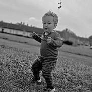 Nico is registered to the contest to win money with this photo: black_and_white, casual_clothing, child, cloudy, curly_hair, daylight, expression, field, grass, leaves, monochrome, nature, outdoor, person, portrait, shoes, sky, toddler, walking, young_child