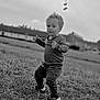 black_and_white, casual_clothing, child, cloudy, curly_hair, daylight, expression, field, grass, leaves, monochrome, nature, outdoor, person, portrait, shoes, sky, toddler, walking, young_child