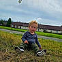 casual_clothing, child, cloudy, curious, curly_hair, daylight, footwear, grass, greenery, houses, leaves, nature, outdoor, portrait, road, sitting, sky, suburban, toddler, young_child