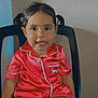 black_chair, buttoned_shirt, chair, child, clothing, cute, face, happy, indoor, person, pigtails, portrait, red_pajamas, seated, shorts, skin, smile, toddler, wall, young_child