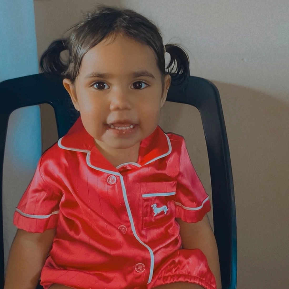 Kytaiviah is registered to the contest to win money with this photo: black_chair, buttoned_shirt, chair, child, clothing, cute, face, happy, indoor, person, pigtails, portrait, red_pajamas, seated, shorts, skin, smile, toddler, wall, young_child