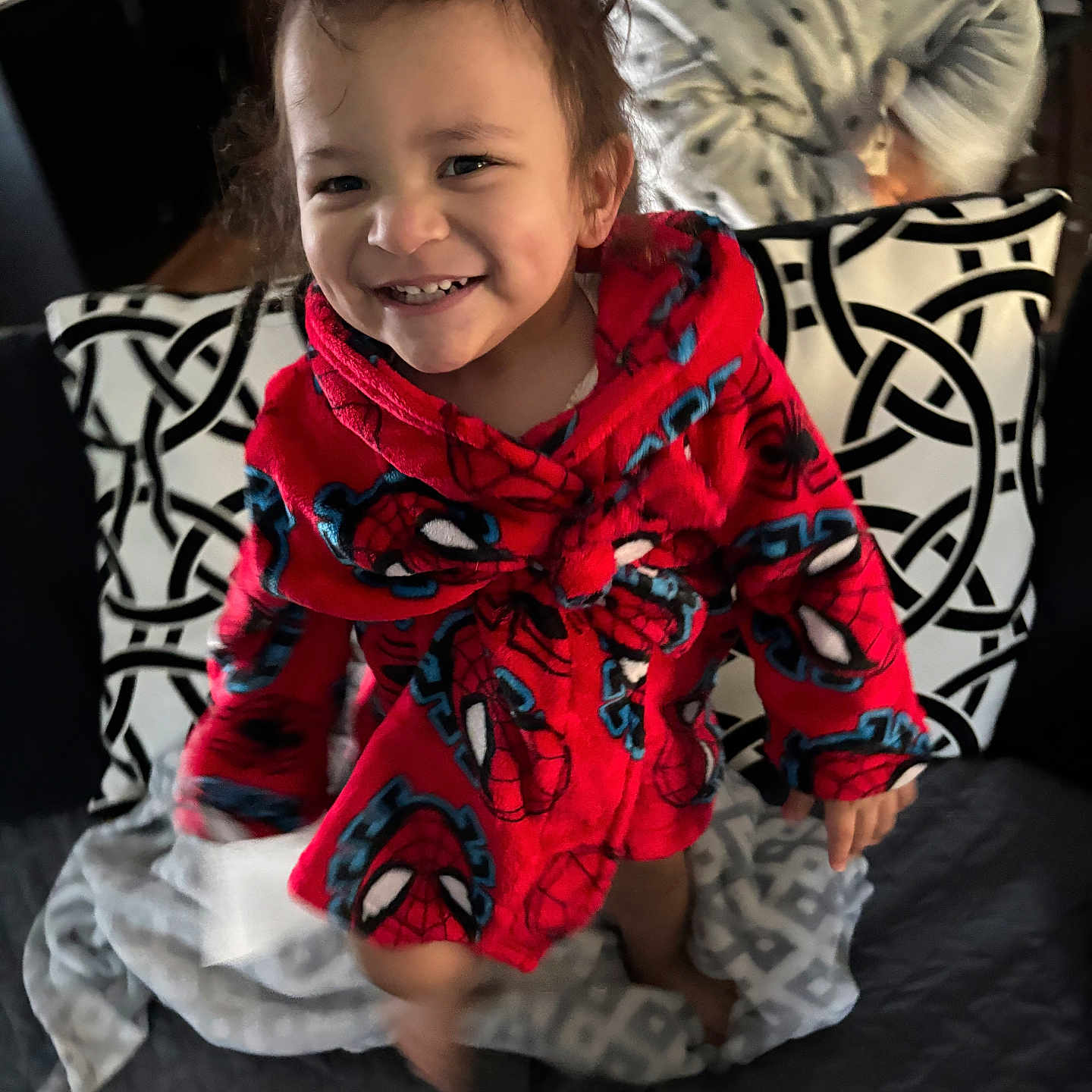 Legend is registered to the contest to win money with this photo: child, toddler, smiling, portrait, spiderman, robe, red_clothing, superhero, blanket, cushion, couch, indoor, home, seated, standing, happy, face, hair, patterned_fabric, photography
