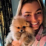 person, dog, pomeranian, puppy, smile, plaid_shirt, indoor, curtain, window, face, fur, pet, portrait, happy, holding, cute, fluffy, animal, cozy, warm_lighting