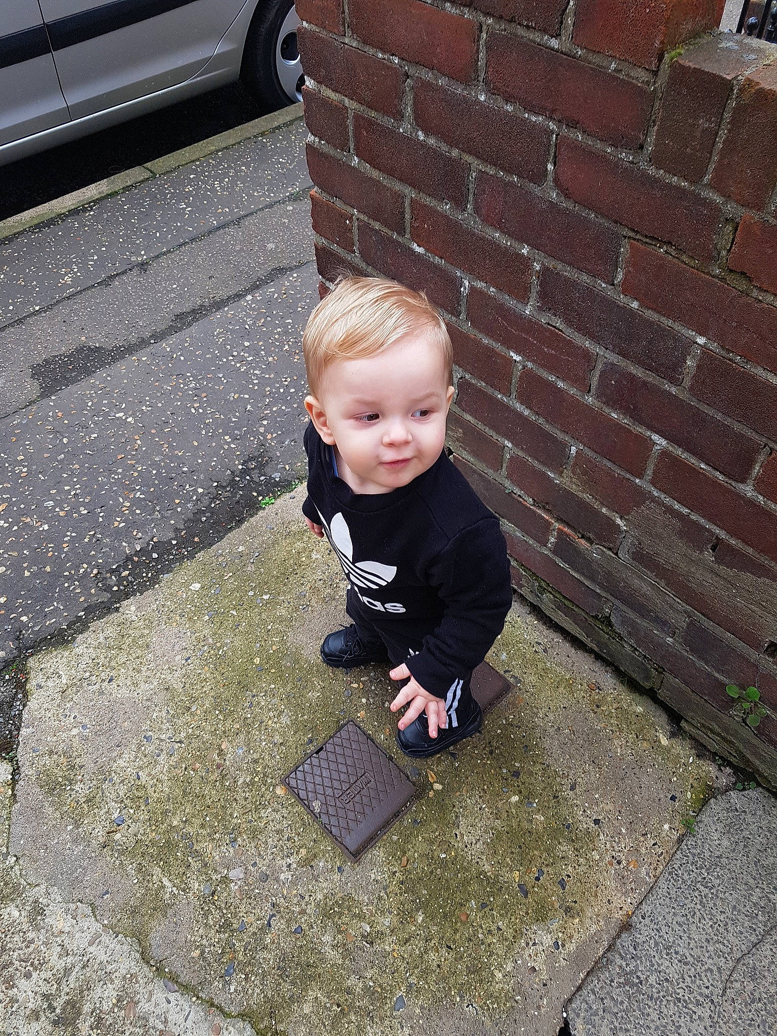 Benny is registered to the contest to win money with this photo: child, cobblestone, floor, flooring, person, play, road_surface, shoe, sitting, smile, square, toddler, vacation