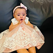 Samriddha is registered to the contest to win money with this photo: baby, child, dress, pink, lace, headband, bow, couch, leather, sitting, chewing, fabric, cute, indoor, person, infant, young_child, happy, portrait, clothing
