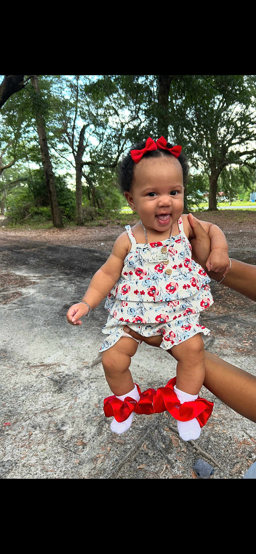 Myla joined the competition — help win amazing prizes! baby, child, smiling, outdoor, trees, nature, greenery, person, red_bow, floral_dress, socks, holding_hand, cute, happy, portrait, grass, sunlight, jewelry, infant, playful