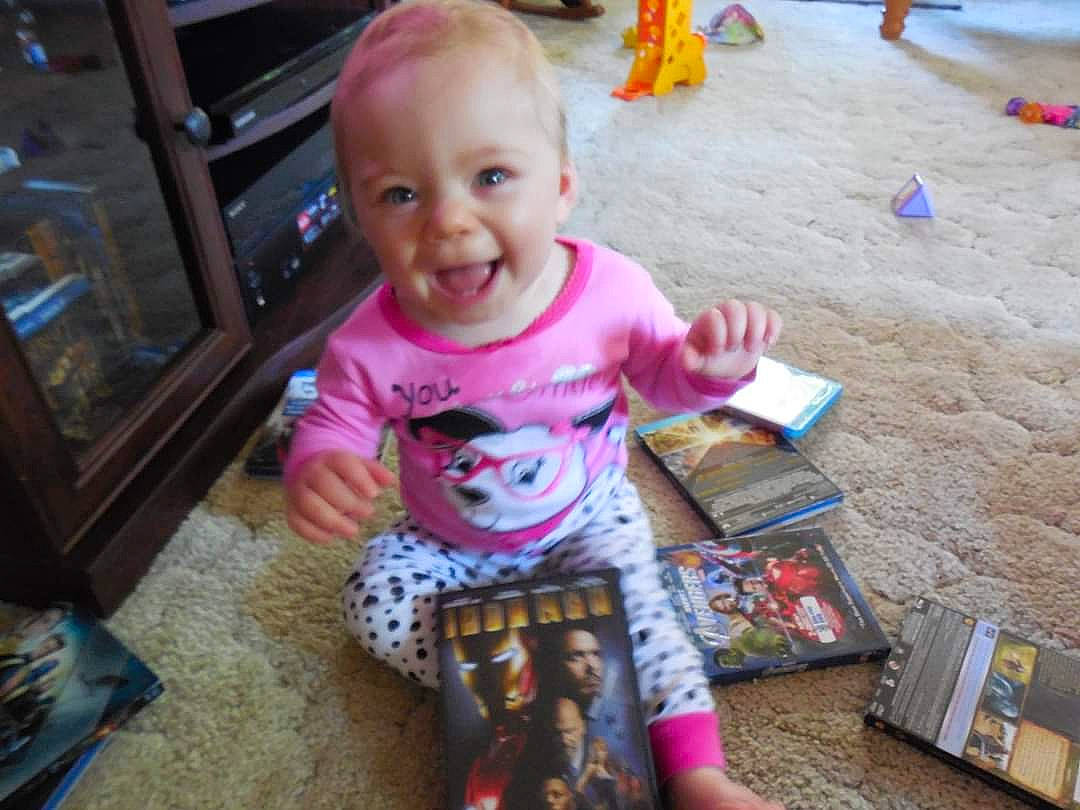 Liliana is registered to the contest to win money with this photo: baby, baby_toddler_clothing, book, cheek, child, flooring, fun, happy, home_appliance, people, person, play, publication, room, sitting, smile, snapshot, t_shirt, toddler, vacation
