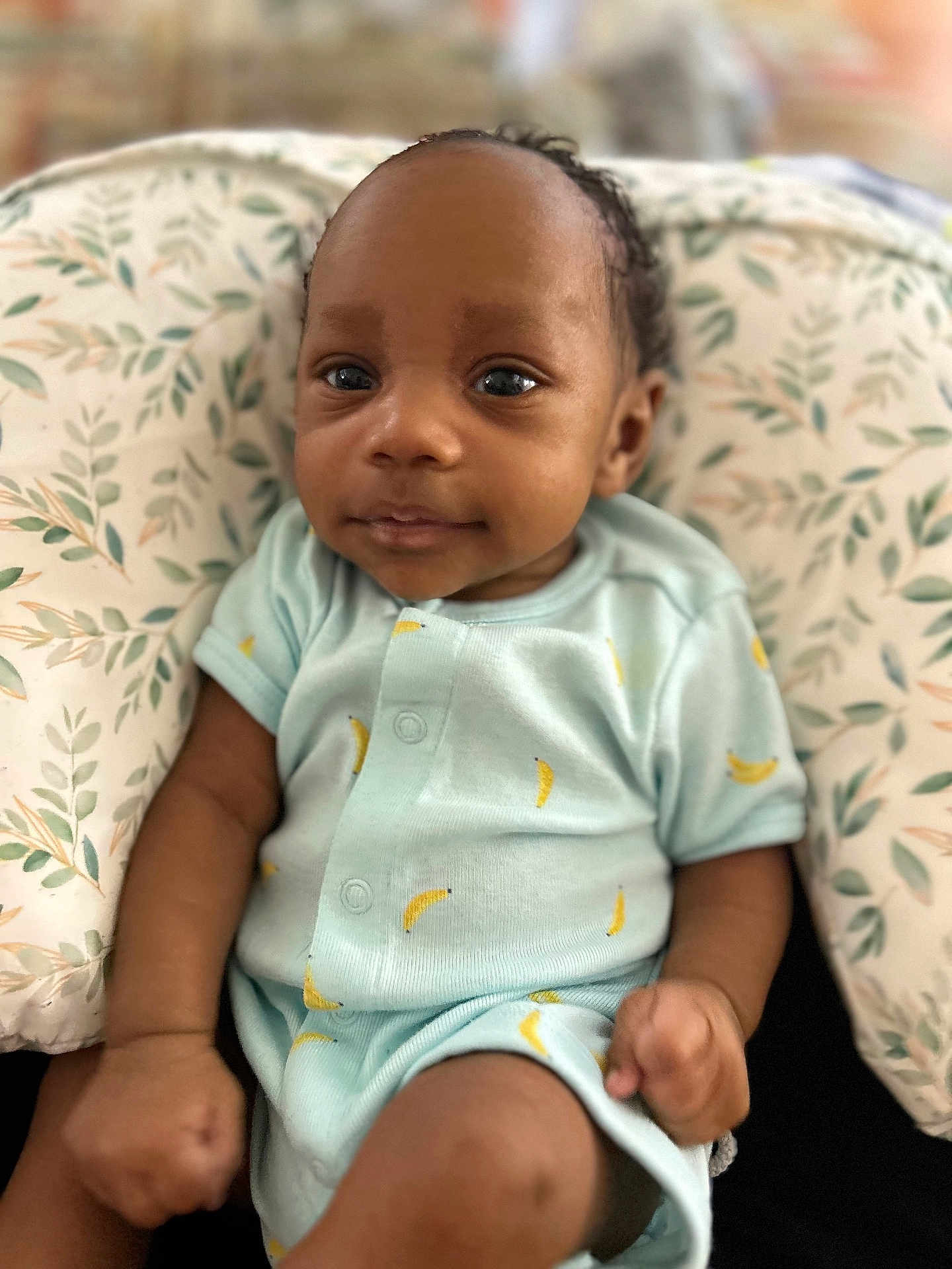 Jelani joined the competition — help win amazing prizes! baby, infant, onesie, blue_clothing, patterned_cushion, leaf_pattern, fist, skin, face, eyes, indoor, comfort, cute, child, newborn, portrait, sitting, young, person, relaxing