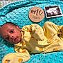 baby, infant, yellow_onesie, orange_patterns, turquoise_blanket, textured_blanket, wooden_sign, one_month, ultrasound_photo, newborn, lying_down, cozy, cute, portrait, indoor, soft_lighting, face, head, sleepwear, child