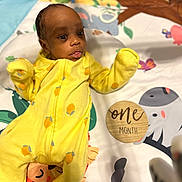 Jelani joined the competition — help win amazing prizes! baby, infant, yellow_onesie, play_mat, animal_print, wooden_plaque, one_month, newborn, cute, lying_down, indoors, child, face, head, expression, soft_lighting, colorful, patterned, milestone, portrait