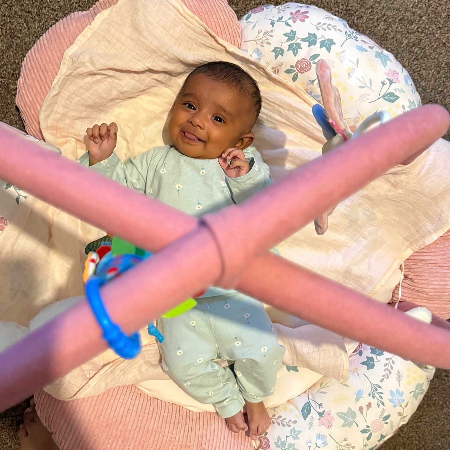 Alza is registered to the contest to win money with this photo: baby, baby_toys, blanket, carpet, child, colorful, cushion, cute, feet, floor, floral_pattern, happy, indoors, infant, lying_down, onesie, playtime, smiling, soft_toys, tongue_out