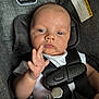 Oaklan is registered to the contest to win money with this photo: baby, infant, car_seat, harness, white_shirt, hand, face, eyes, skin, warning_label, gray_fabric, close_up, seat_belt, clip, pacifier_clip, child, indoors, portrait, young_child, evenflo
