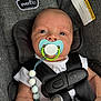 baby, pacifier, car_seat, harness, white_shirt, beaded_pacifier_clip, close_up, infant, child, seatbelt, gray_fabric, safety_label, clip, straps, child_safety, cute, portrait, indoors, person, baby_accessory