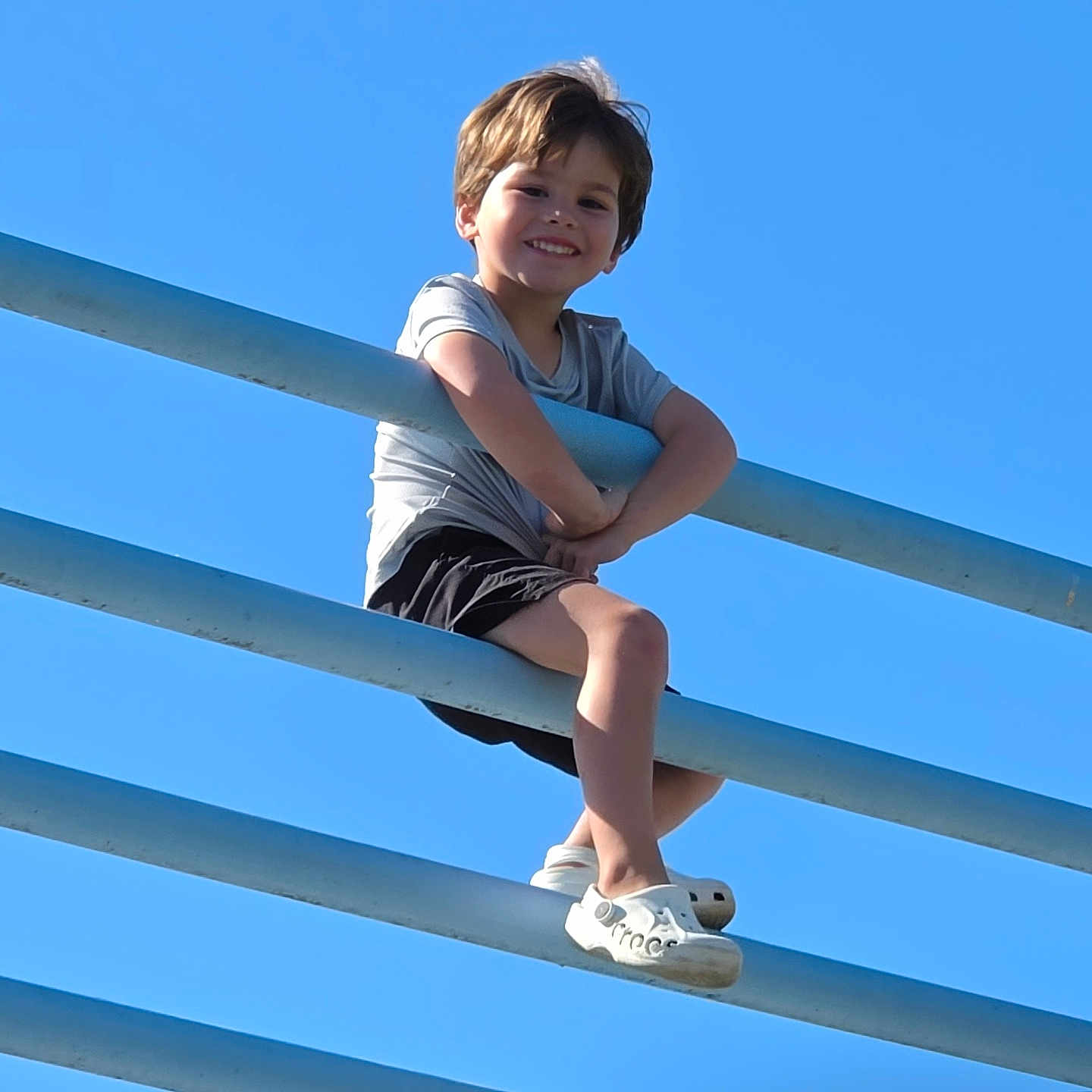 Tatum joined the competition — help win amazing prizes! child, smiling, outdoor, playground, railings, blue_sky, sunlight, portrait, sitting, climbing, acrobatics, gray_shirt, black_shorts, white_shoes, brown_hair, happy, summer, daylight, low_angle, adventure
