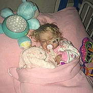 Eve Mae is registered to the contest to win money with this photo: toddler, sleeping, blanket, stuffed_animal, toy, bed, pacifier, cozy, child, plush, indoor, pink, blue, nighttime, quiet, rest, comfort, pajamas, hospital_bed, medical_tape