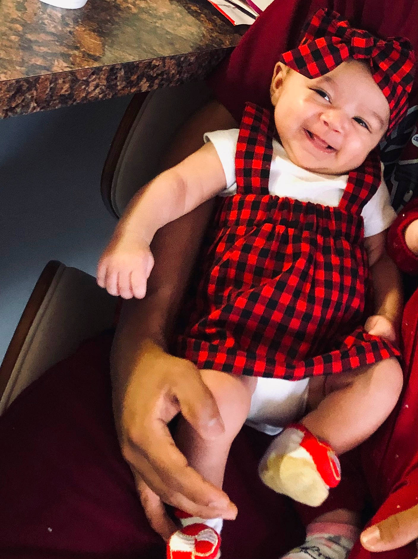 Xiomara is registered to the contest to win money with this photo: baby, baby_products, baby_toddler_clothing, bonnet, carmine, child, costume_accessory, fictional_character, hand, headwear, lamp, lap, laugh, pattern, person, plaid, pleased, sitting, sock, tartan