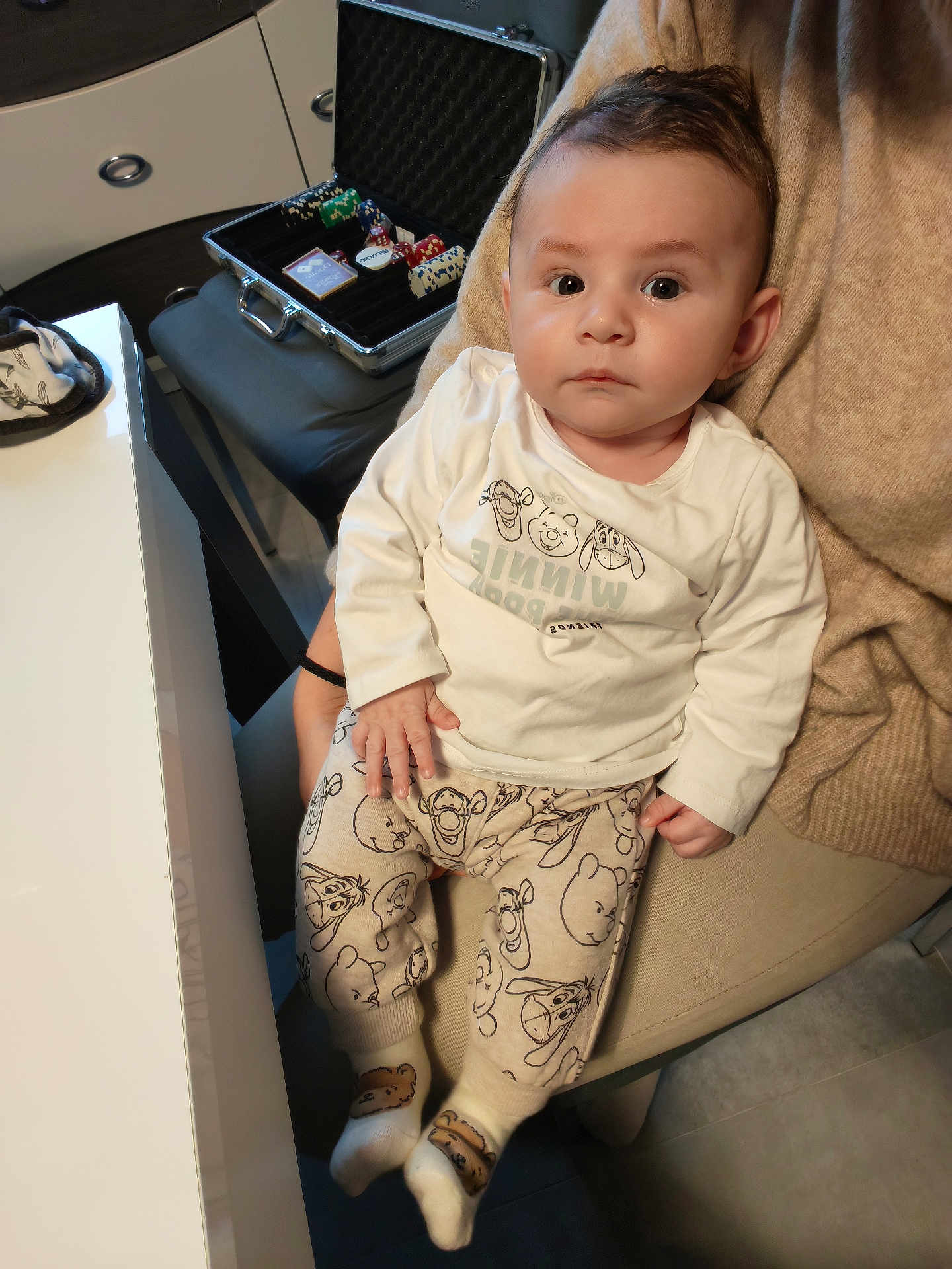 Adam participe au concours pour gagner de l'argent avec cette photo : baby, child, indoor, clothing, winnie_the_pooh, pajamas, person, face, seat, chair, hand, footwear, socks, table, poker_chips, playing_cards, curious, portrait, cute, expression