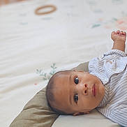 Juliann a rejoint le concours — aidez-le/la à gagner de superbes lots ! baby, infant, face, eyes, clothing, striped_shirt, cushion, bed, blanket, indoor, portrait, person, child, young, skin, head, expression, curious, laying, soft