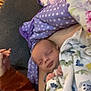 Quentin is registered to the contest to win money with this photo: baby, blanket, couch, person, sleeping, infant, purple_blanket, polka_dots, dinosaur_pattern, hand, orange_clothing, cozy, indoor, resting, child, soft_fabric, comfort, relaxation, peaceful, home