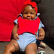 Senora joined the competition — help win amazing prizes! baby, infant, smile, red_bib, headband, couch, cushion, happy, child, indoor, legs, clothing, pacifier, strap, skin, face, sitting, relaxing, cute, comfortable