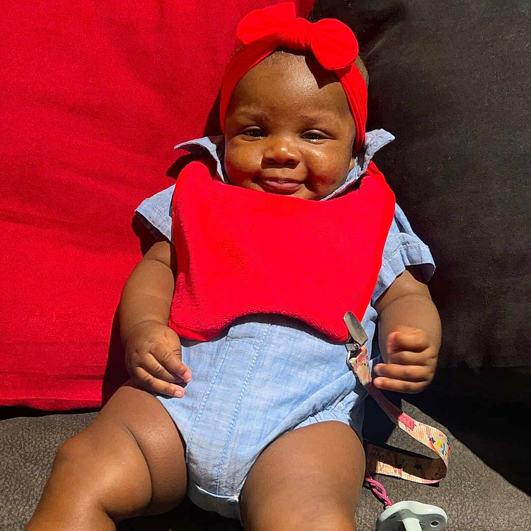 Senora joined the competition — help win amazing prizes! baby, child, clothing, comfortable, couch, cushion, cute, face, happy, headband, indoor, infant, legs, pacifier, red_bib, relaxing, sitting, skin, smile, strap