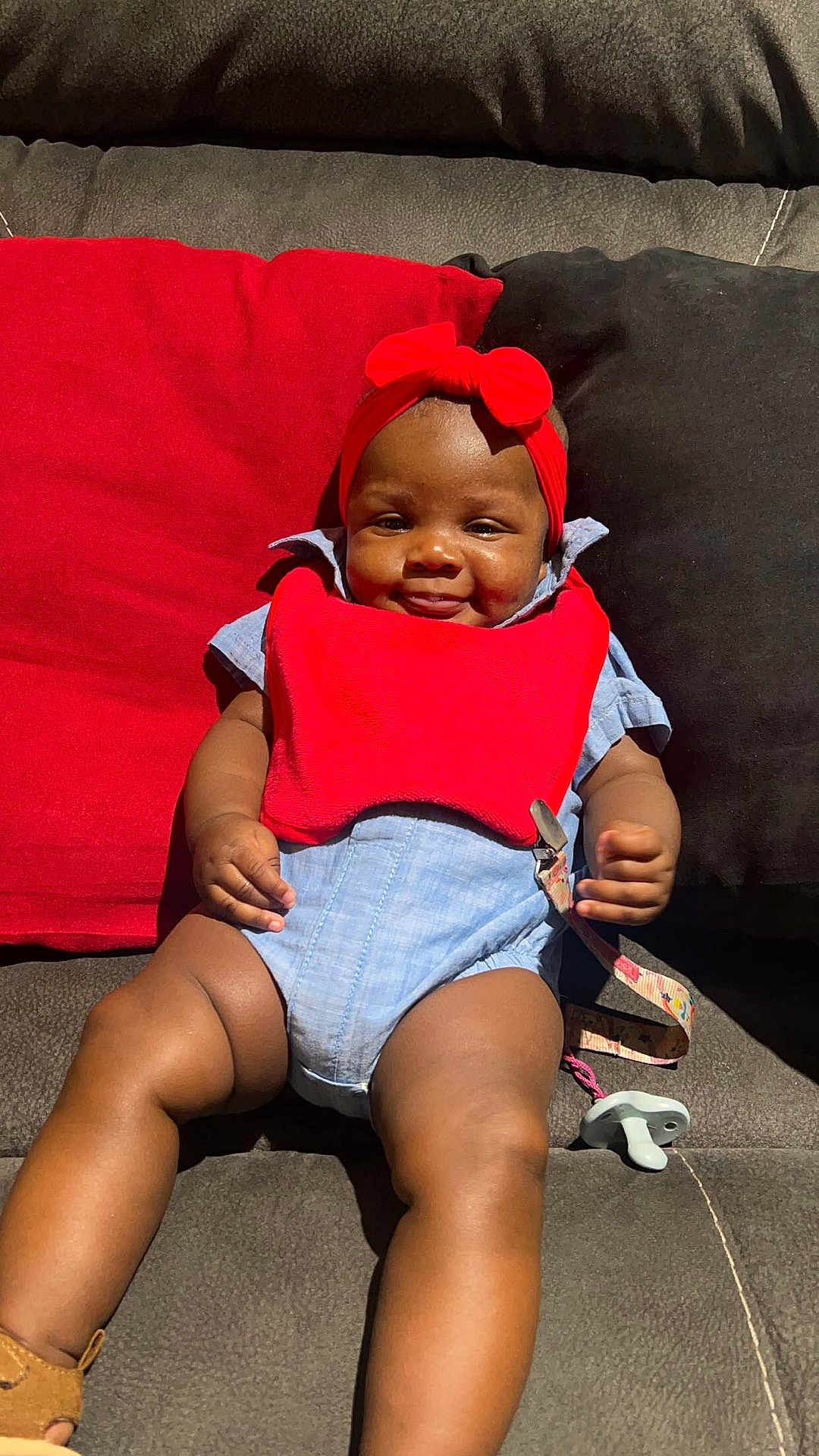 Senora joined the competition — help win amazing prizes! baby, infant, smile, red_bib, headband, couch, cushion, happy, child, indoor, legs, clothing, pacifier, strap, skin, face, sitting, relaxing, cute, comfortable