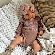 Mila is registered to the contest to win money with this photo: baby, blanket, bow, child, clothing, couch, cozy, cute, face, headwrap, indoors, infant, infant_girl, onesie, person, portrait, relaxing, smile, socks, soft_texture