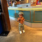 Leslie is registered to the contest to win money with this photo: toddler, child, hat, shorts, sneakers, gold_chain, indoor, floor, counter, cafe, curious, standing, fashion, baby, person, clothing, footwear, concrete_floor, menu, casual