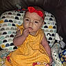 baby, child, infant, dress, headband, red_bow, yellow_dress, crocheted_blanket, cushion, leather_sofa, foot, hand, face, seated, indoors, portrait, curious, cute, soft_toys, colorful