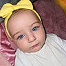 baby, infant, child, portrait, close_up, face, blue_eyes, yellow_bow, headband, white_clothing, lying_down, blanket, bed, indoors, cozy, adorable, looking_at_camera, photography, pink_fabric, soft_lighting