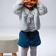 Alba a rejoint le concours — aidez-le/la à gagner de superbes lots ! bow_headband, cat_mask, child, curly_hair, denim_shorts, fashion, hands_up, mask, minimal_background, playful, playful_pose, portrait, smiling, sneakers, standing, stool, studio, tights, toddler, white_jacket