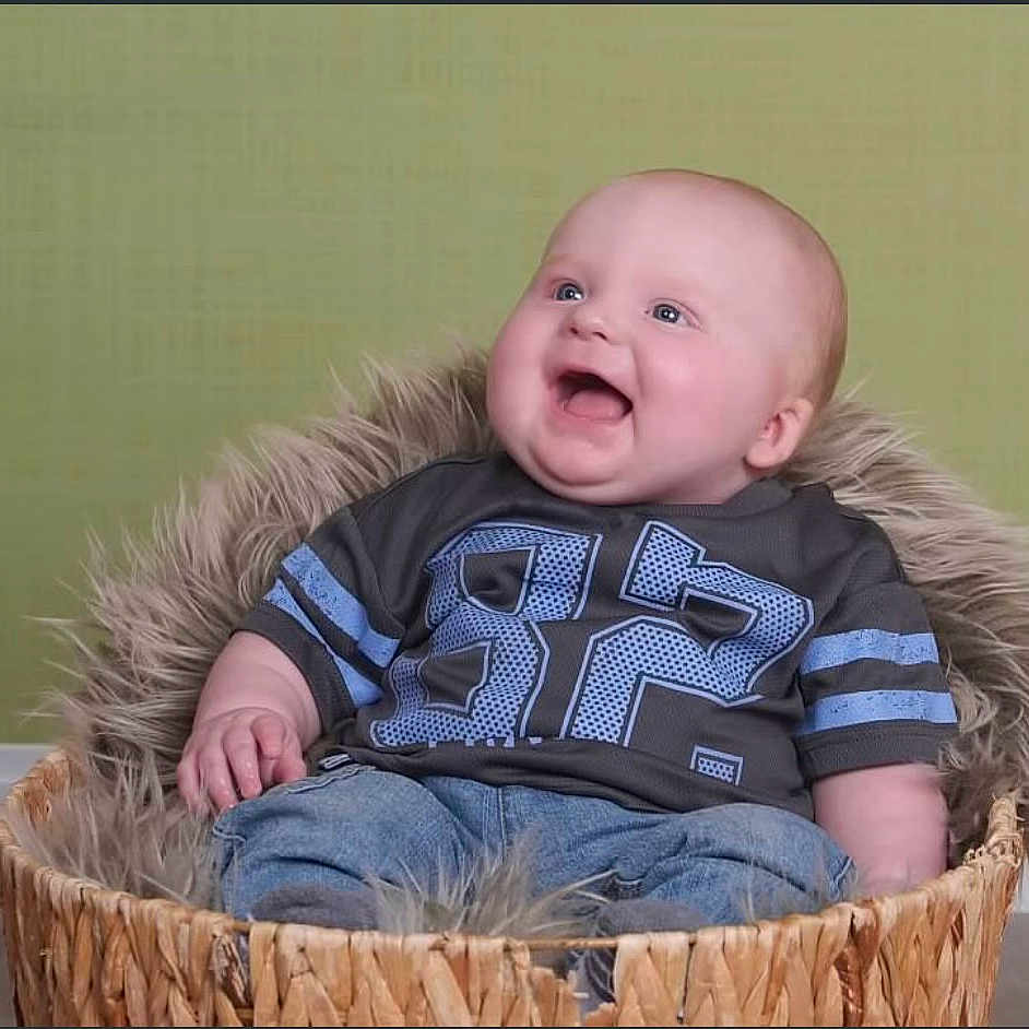 Lucious is registered to the contest to win money with this photo: baby, basket, blue_jeans, clothing, cute, furry, happy, indoor, infant, jeans, joyful, looking_up, person, portrait, shirt, sitting, smile, toddler, woven_basket, young_child
