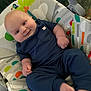 baby, infant, smiling, blue_clothing, baby_seat, colorful_pattern, toucan, indoor, cute, chubby_cheeks, relaxing, child, person, portrait, happy, baby_toys, comfort, seat, foot, hand