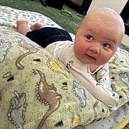 Lucious is registered to the contest to win money with this photo: baby, blanket, dinosaur_pattern, carpet, floor, infant, child, indoor, crawling, cute, clothing, white_shirt, blue_shorts, soft_texture, home, playtime, young, face, expression, person