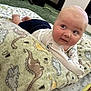 baby, blanket, dinosaur_pattern, carpet, floor, infant, child, indoor, crawling, cute, clothing, white_shirt, blue_shorts, soft_texture, home, playtime, young, face, expression, person