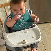 Ezra joined the competition — help win amazing prizes! toddler, child, high_chair, messy, food, bib, eating, smiling, bare_feet, wooden_chair, floor_tiles, indoor, baby, face, hands, clothing, feeding, cute, infant, meal_time