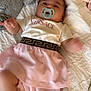 baby, pacifier, blanket, plush_toy, clothing, pink_skirt, white_shirt, infant, bed, soft_toys, cute, sleepwear, child, lying_down, indoor, fabric, comfort, small_child, motion_blur, versace